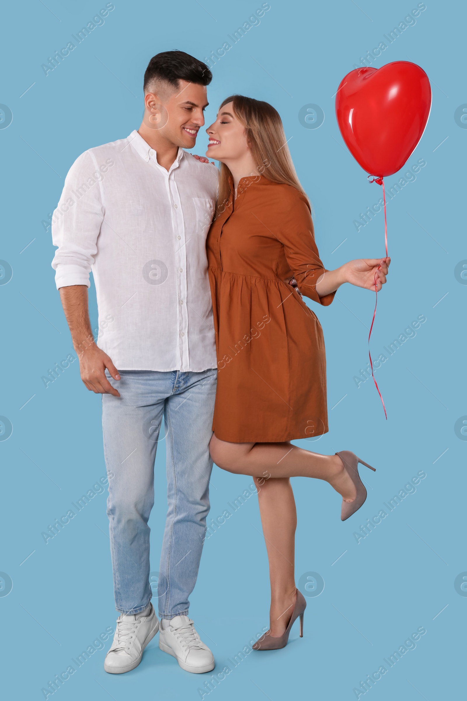 Photo of Lovely couple with heart shaped balloon on light blue background. Valentine's day celebration