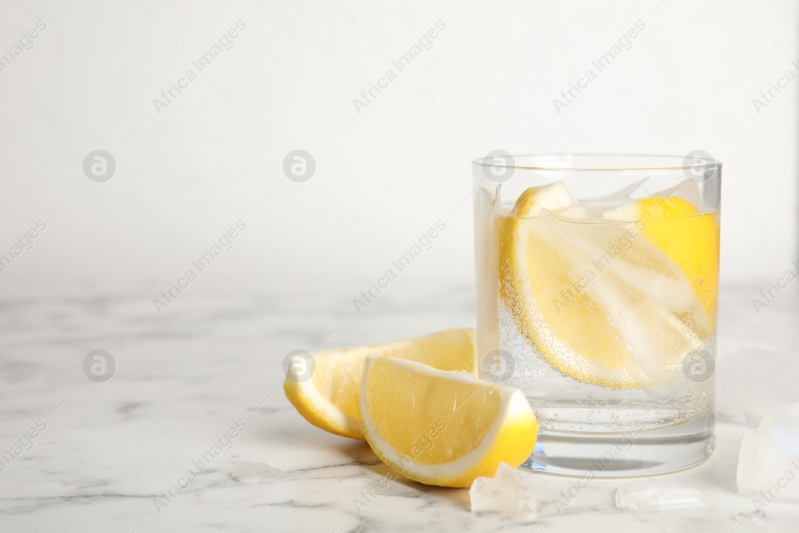 Photo of Soda water with lemon slices and ice cubes on white marble table. Space for text