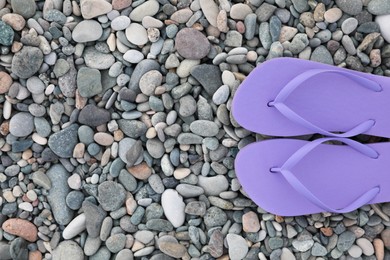 Stylish violet flip flops on pebble seashore, top view. Space for text