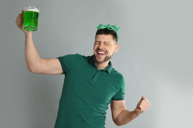 Emotional man in St Patrick's Day outfit with beer on light grey background
