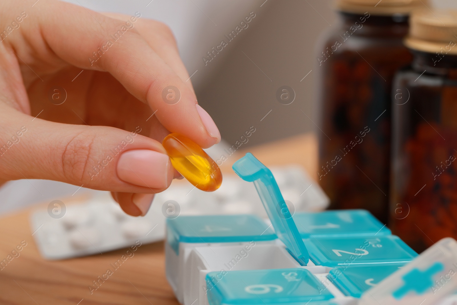 Photo of Woman taking pill from plastic box at wooden table, closeup