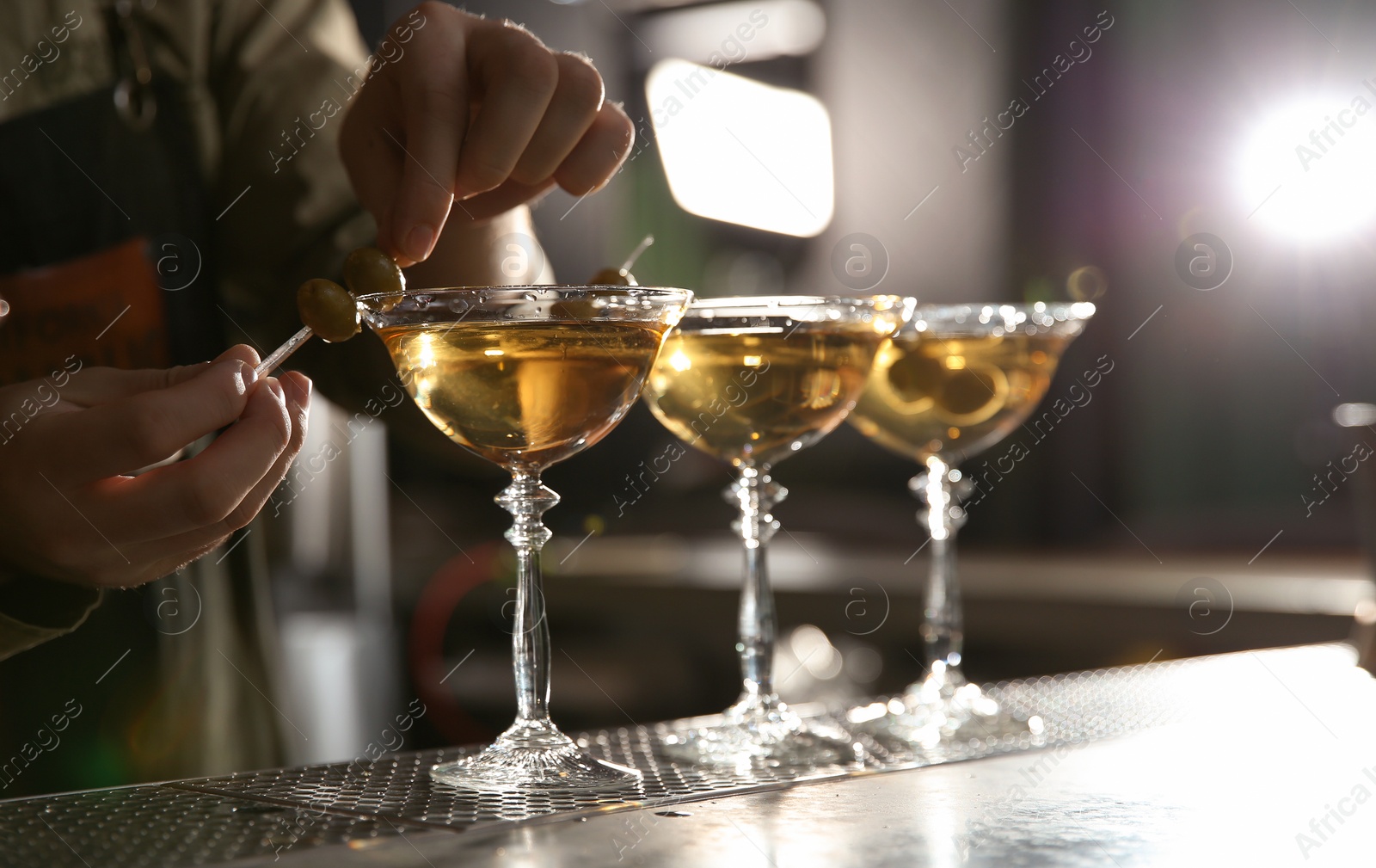 Photo of Barman adding olives to martini cocktail on counter, closeup. Space for text