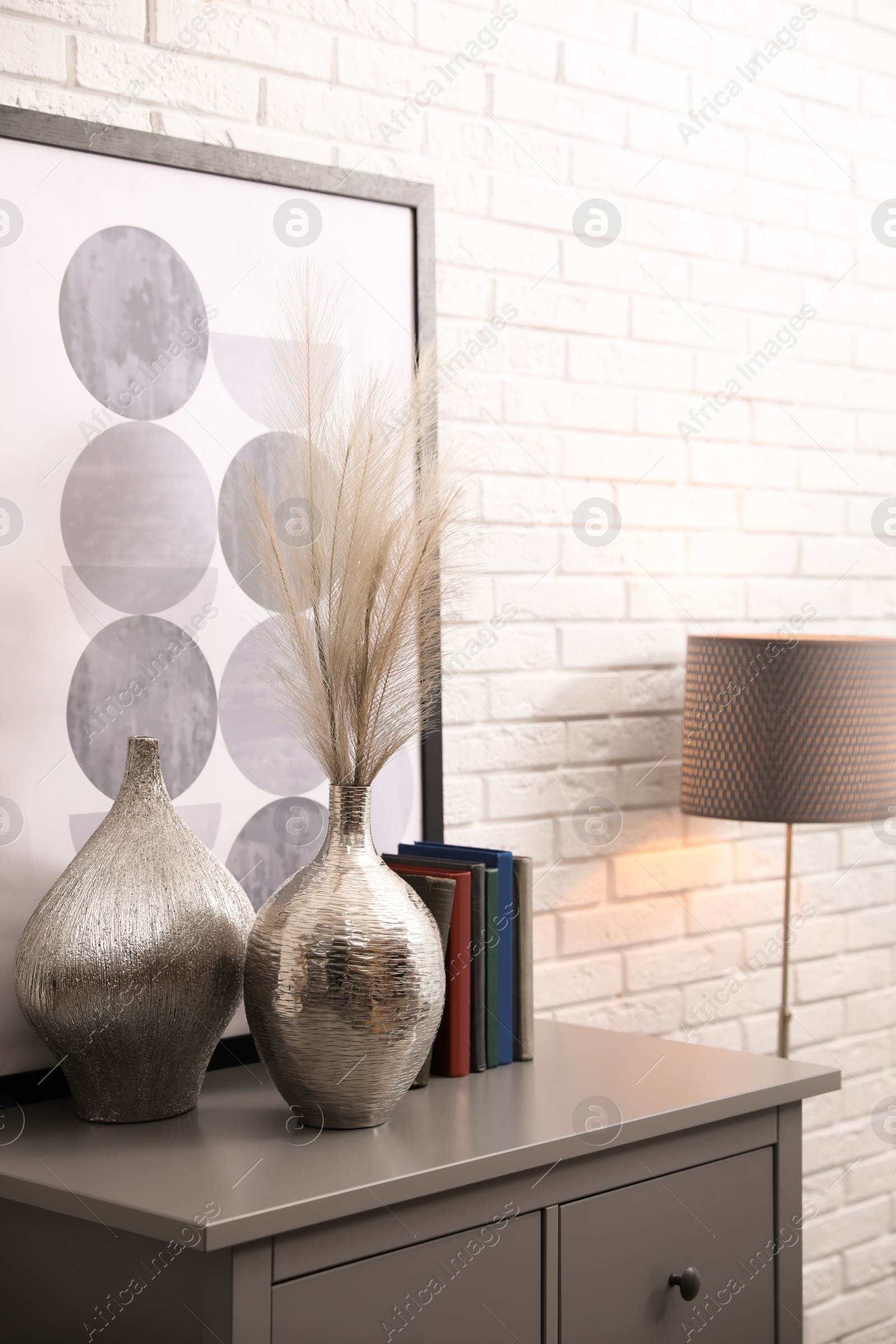 Photo of Grey chest of drawers with decor and books near white brick wall. Interior design