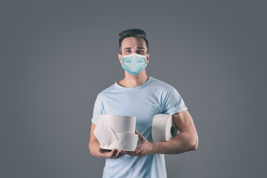 Image of Man in medical mask holding toilet paper rolls on grey background