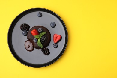 Photo of Plate with delicious chocolate fondant, berries and mint on yellow table, top view. Space for text