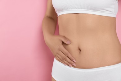 Photo of Woman in underwear touching her belly on pink background, closeup. Healthy stomach