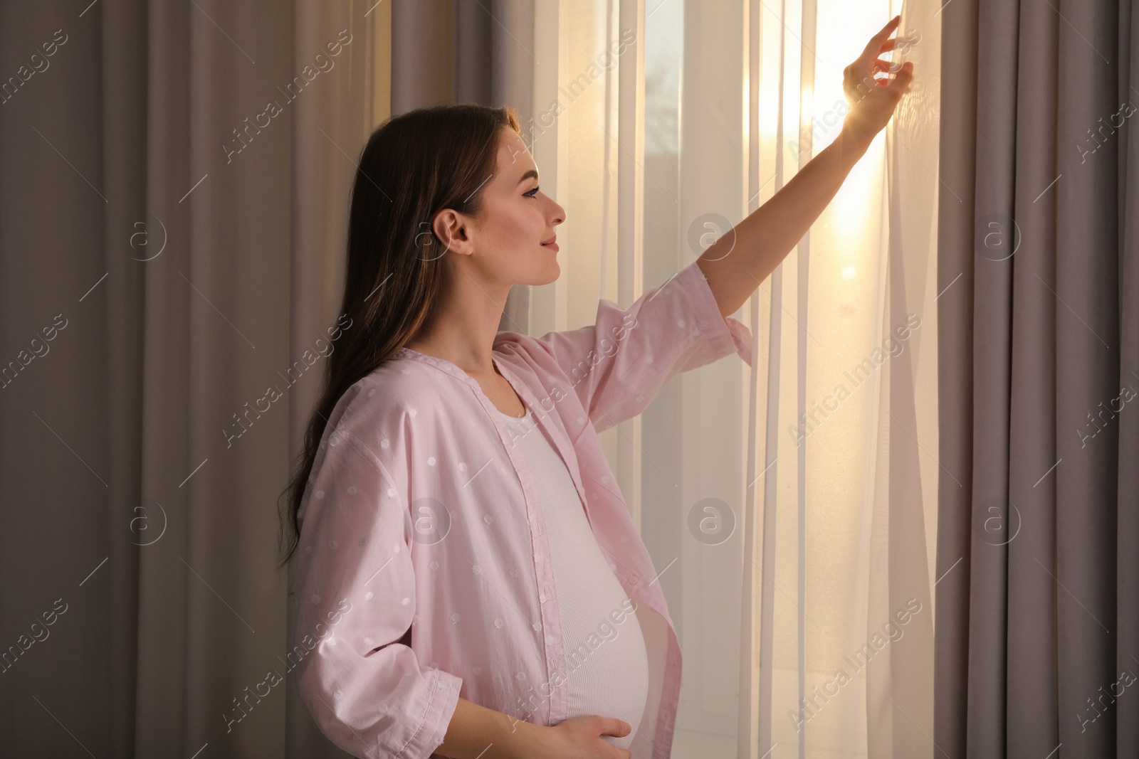 Photo of Young pregnant woman near window at home