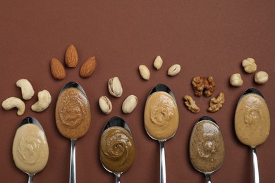 Photo of Tasty nut butters in spoons and raw nuts on brown table, flat lay. Space for text