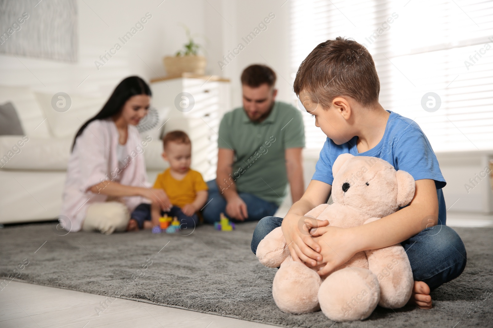 Photo of Unhappy little boy feeling jealous while parents spending time with his baby brother at home