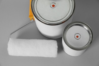 Cans of orange paint and roller brush on grey background, above view