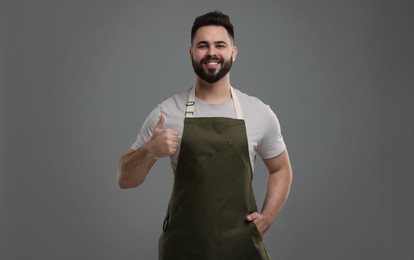 Photo of Smiling man in kitchen apron showing thumb up on grey background. Mockup for design
