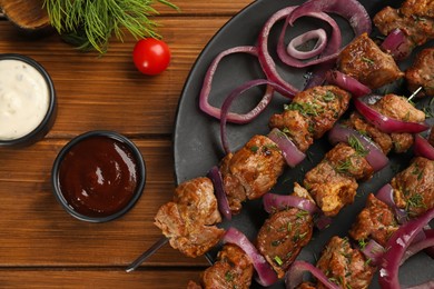 Photo of Metal skewers with delicious meat, onion and ketchup served on wooden table, flat lay