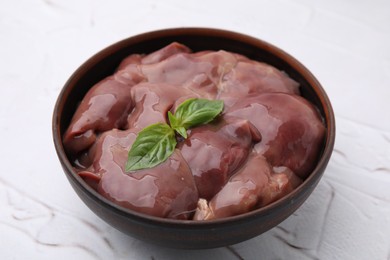 Photo of Bowl with raw chicken liver and basil on white textured table, closeup