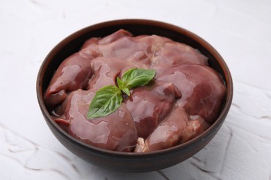 Bowl with raw chicken liver and basil on white textured table, closeup