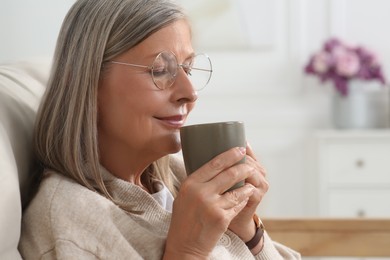Photo of Beautiful senior woman drinking tea on sofa at home, space for text