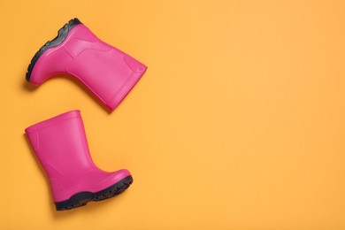 Photo of Pair of bright pink rubber boots on orange background, top view. Space for text