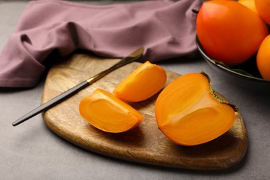 Photo of Delicious ripe persimmons and knife on wooden board, closeup