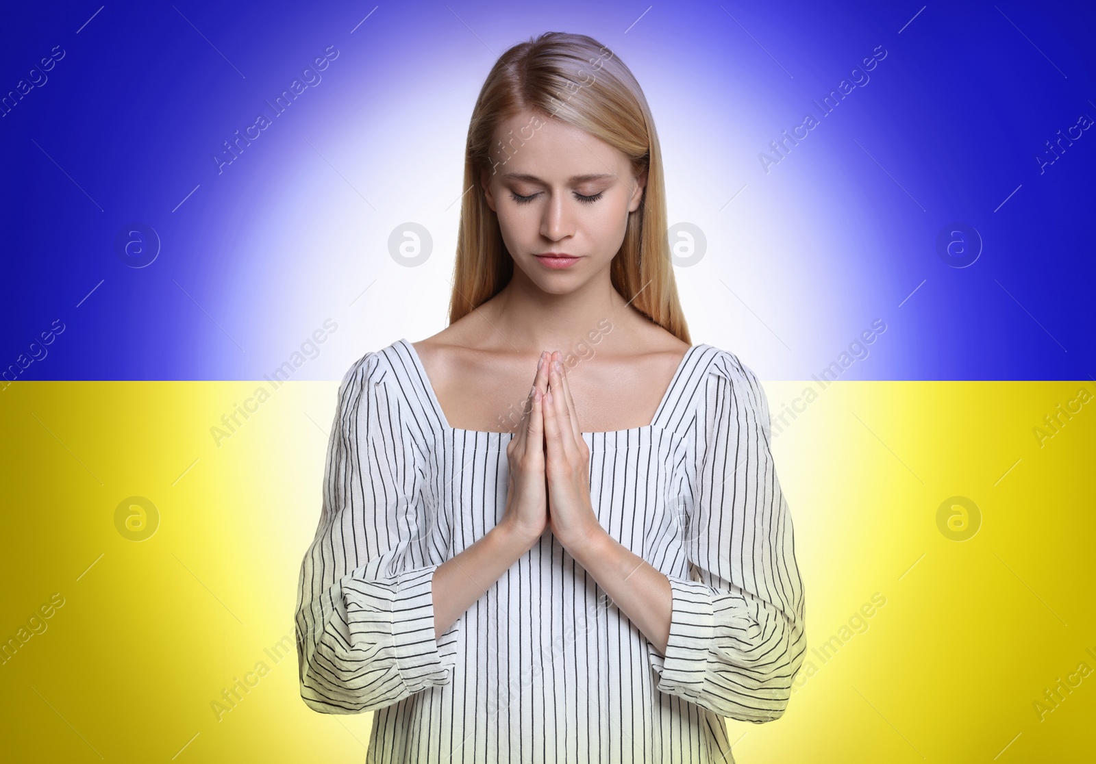Image of Pray for Ukraine. Young woman with clasped hands praying against Ukrainian national flag