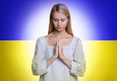 Pray for Ukraine. Young woman with clasped hands praying against Ukrainian national flag