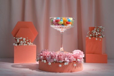 Photo of Stylish presentation of glass with candies, gypsophila and carnation flowers on pink marble table