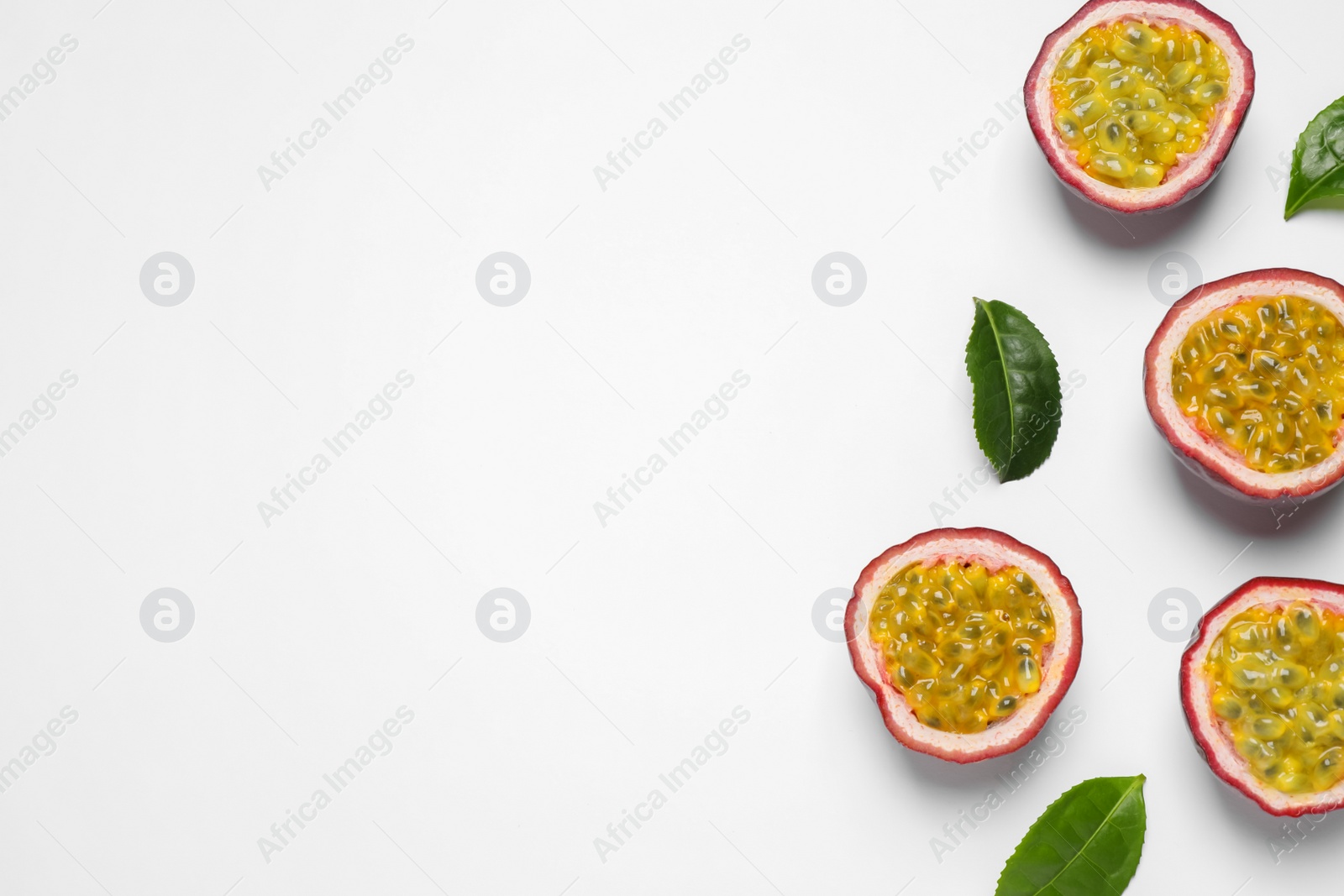 Photo of Halves of passion fruits (maracuyas) and green leaves on white background, flat lay. Space for text