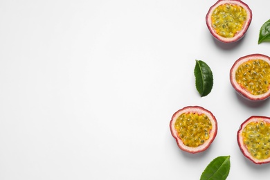 Halves of passion fruits (maracuyas) and green leaves on white background, flat lay. Space for text