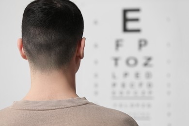 Photo of Eyesight examination. Young man looking at vision test chart indoors, back view