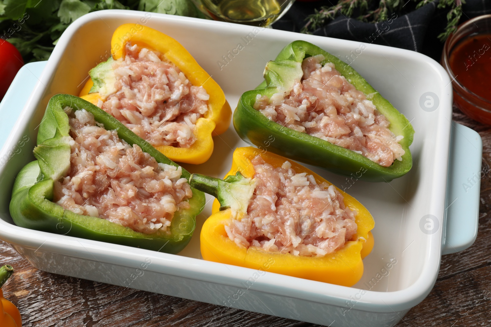Photo of Raw stuffed peppers in dish on wooden table, closeup
