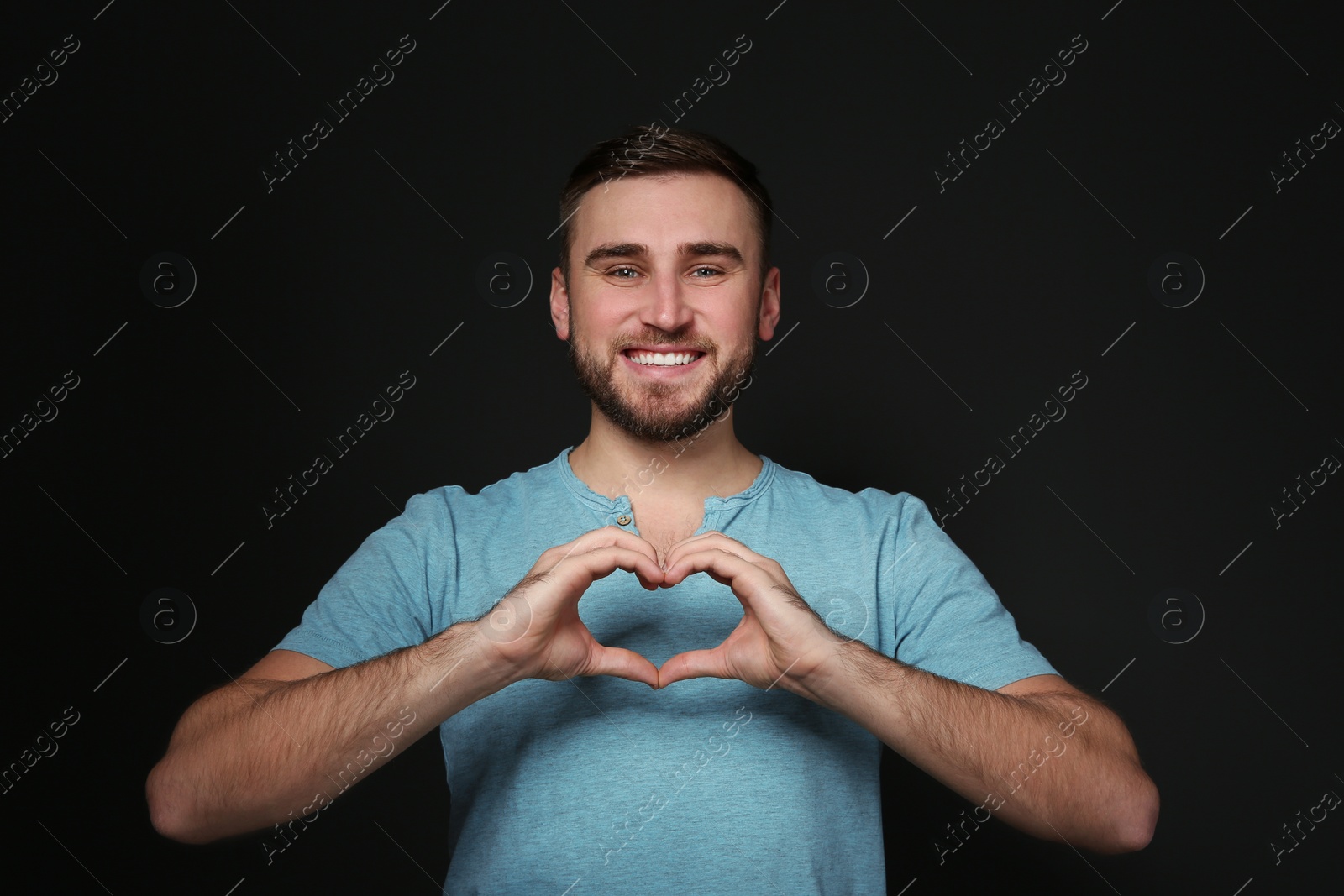 Photo of Man showing HEART gesture in sign language on black background