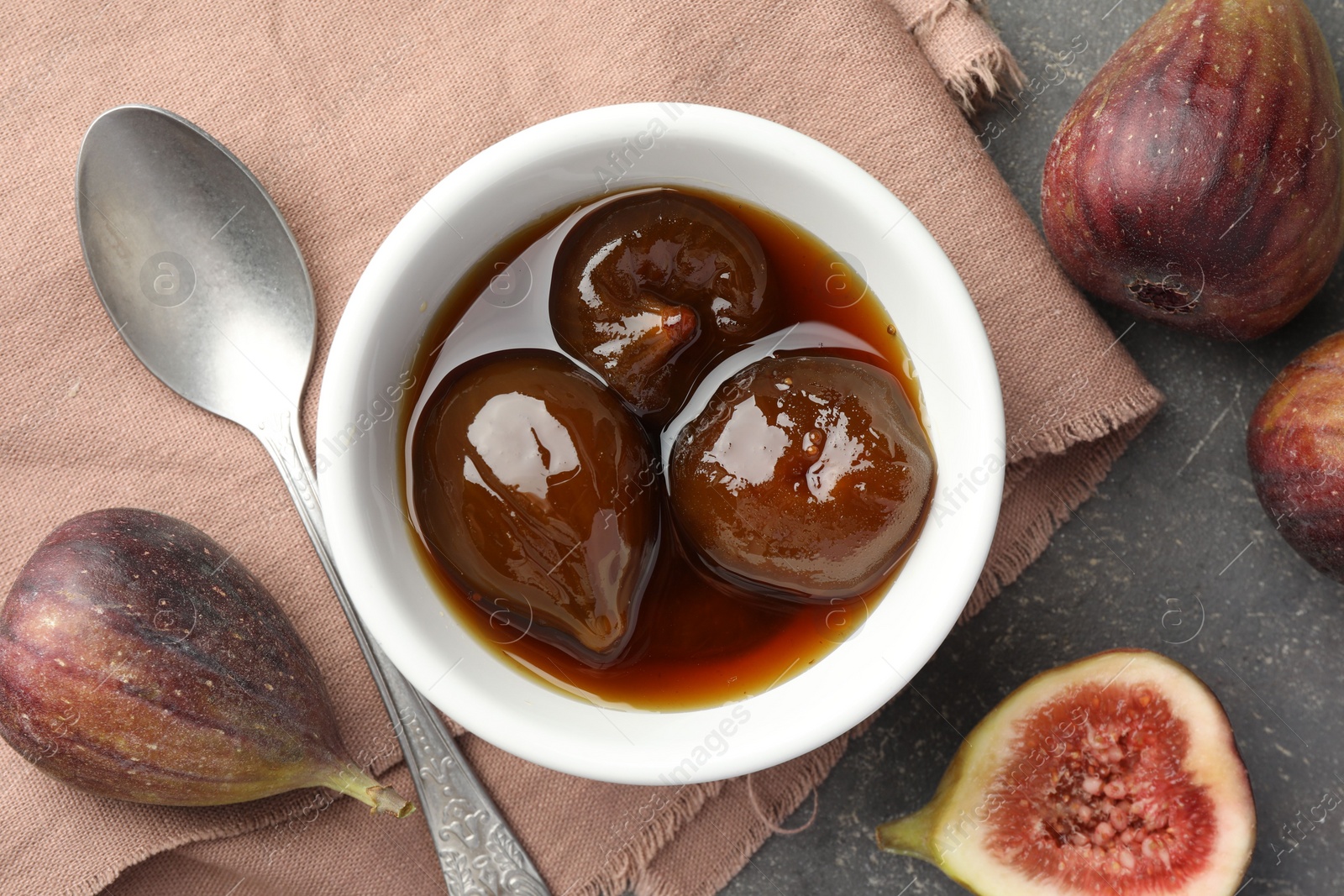 Photo of Bowl of tasty sweet jam, fresh figs and spoon on grey table, flat lay