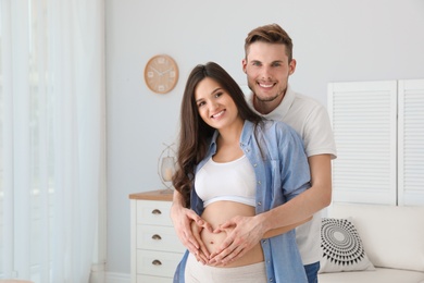 Pregnant woman and her husband showing heart with hands at home