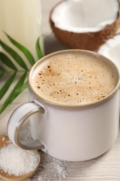 Photo of Cup of coffee, halves of coconut, flakes and green leaves on white wooden table, closeup
