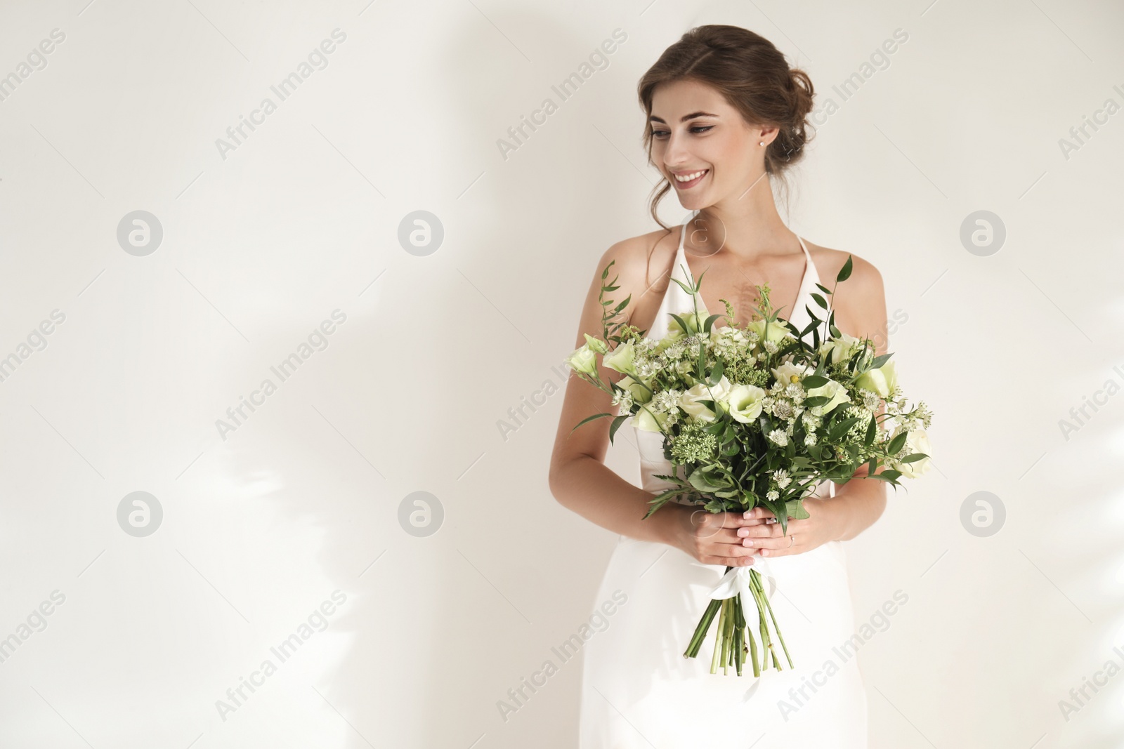 Photo of Young bride wearing wedding dress with beautiful bouquet on light background. Space for text