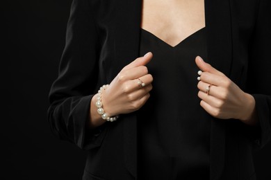 Young woman with elegant pearl jewelry on black background, closeup