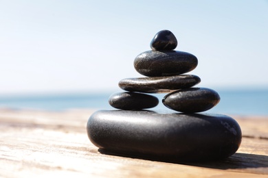 Photo of Stack of stones on wooden pier near sea, space for text. Zen concept