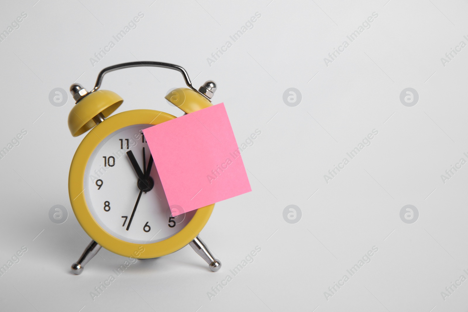 Photo of Alarm clock and blank reminder note on light grey background. Space for text