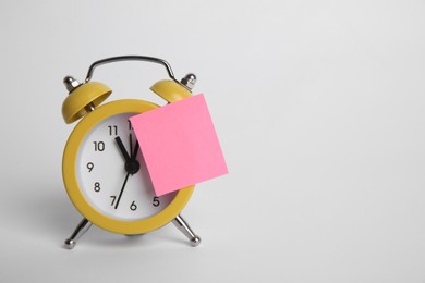 Alarm clock and blank reminder note on light grey background. Space for text