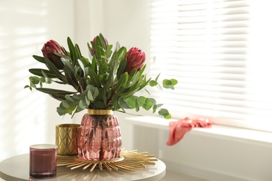 Vase with bouquet of beautiful Protea flowers on table in room