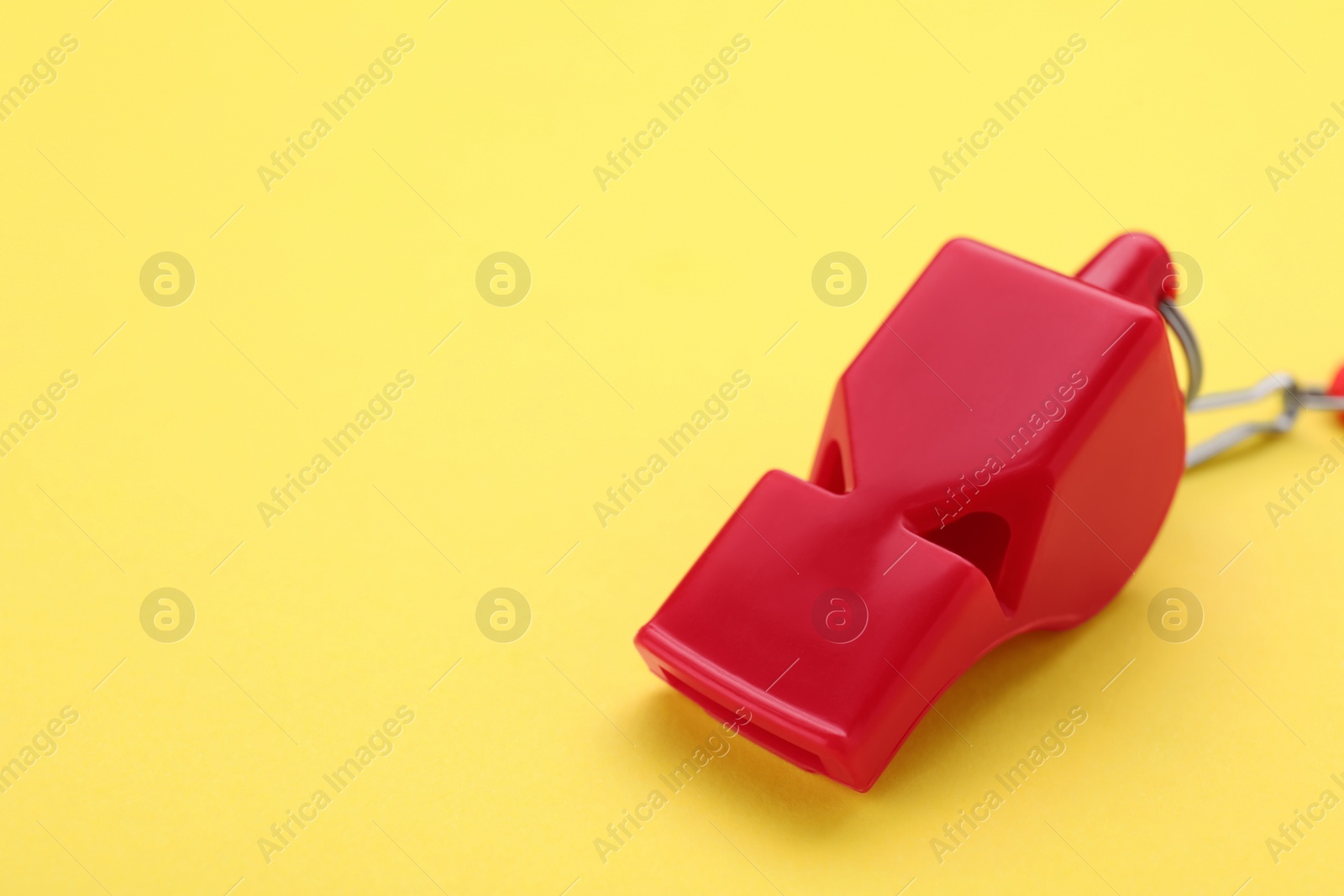 Photo of One red whistle on yellow background, closeup. Space for text