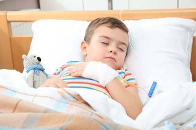 Photo of Little child with intravenous drip sleeping in hospital bed