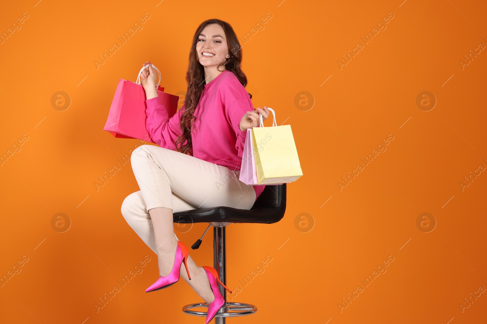 Photo of Happy woman holding colorful shopping bags on chair against orange background