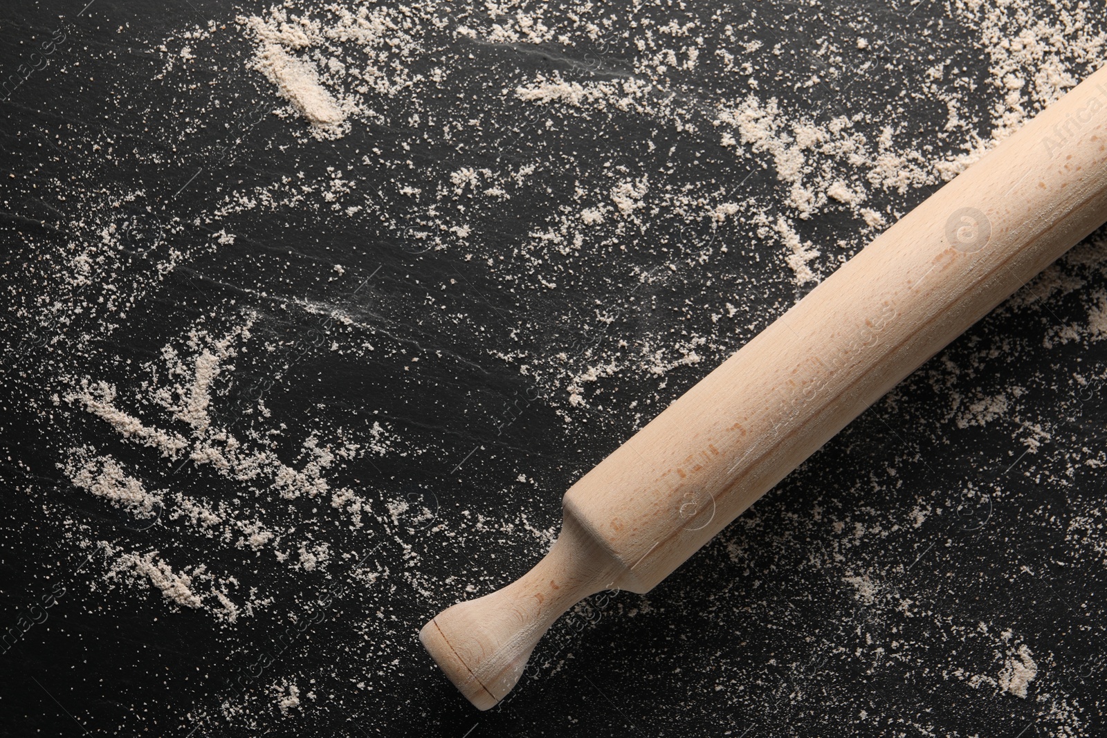 Photo of Scattered flour and rolling pin on black textured table, top view