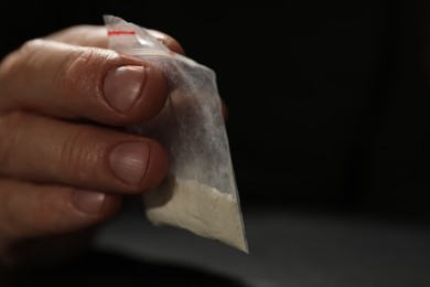 Photo of Addicted man with plastic bag of hard drug on dark background, closeup. Space for text