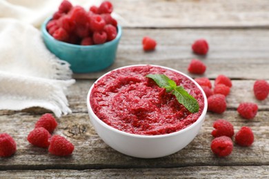 Photo of Raspberry puree in bowl and fresh berries on wooden table