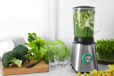 Photo of Blender with delicious smoothie and ingredients in kitchen