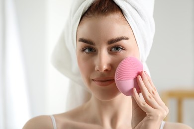 Washing face. Young woman with cleansing brush indoors