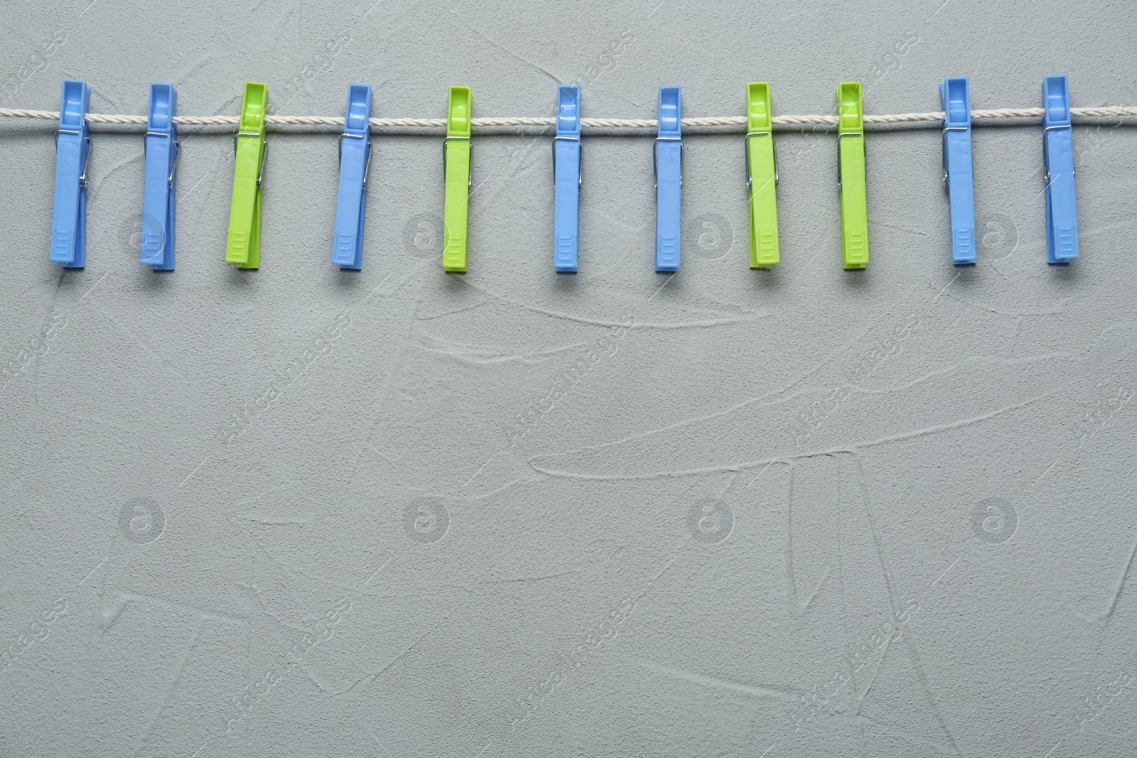 Photo of Colorful plastic clothespins and rope on light grey stone background. Space for text