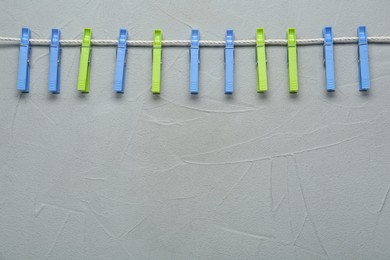 Photo of Colorful plastic clothespins and rope on light grey stone background. Space for text