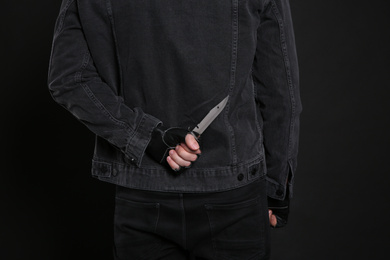 Photo of Man with knife behind his back on black background, closeup. Dangerous criminal