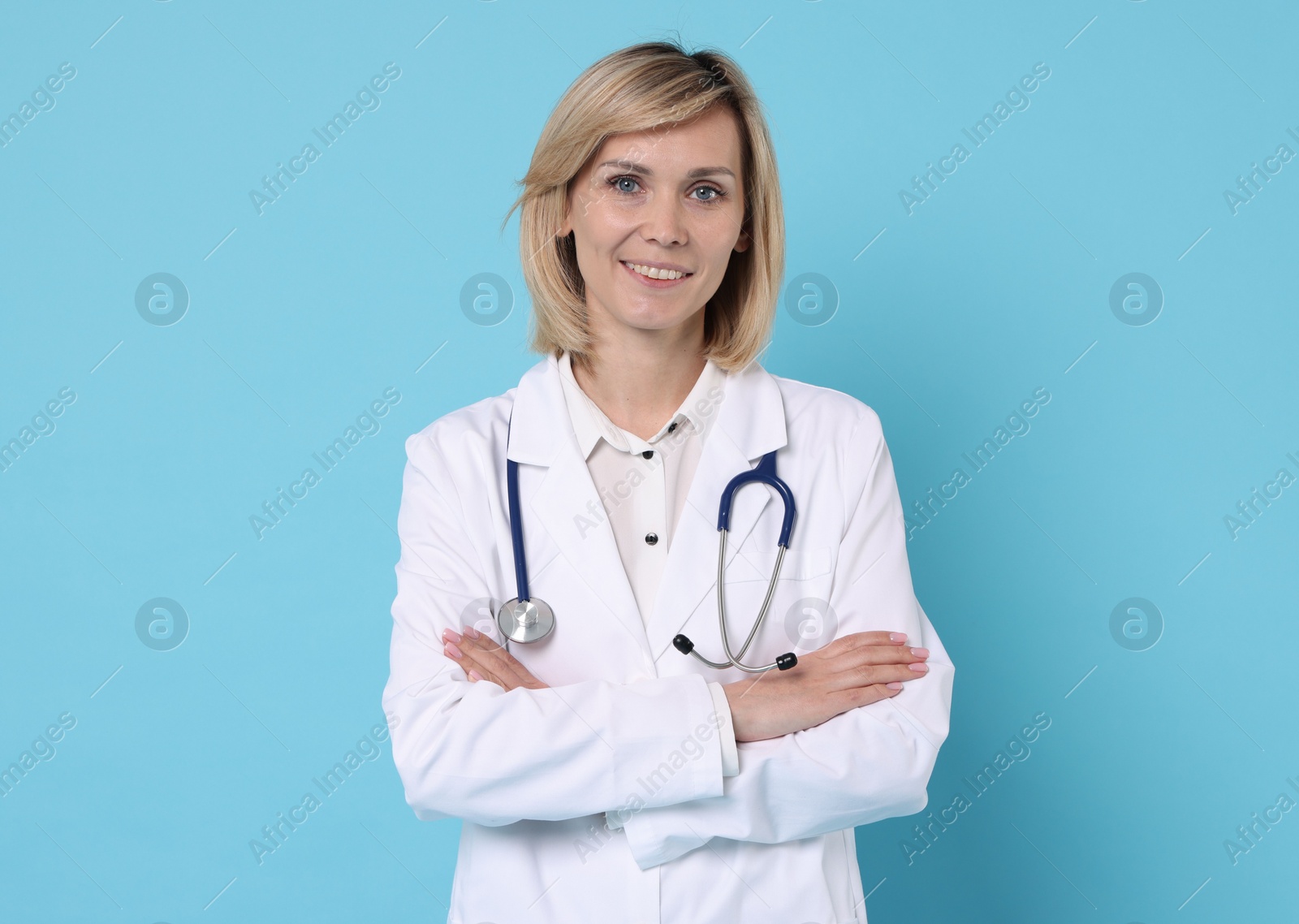 Photo of Smiling doctor with crossed arms on light blue background